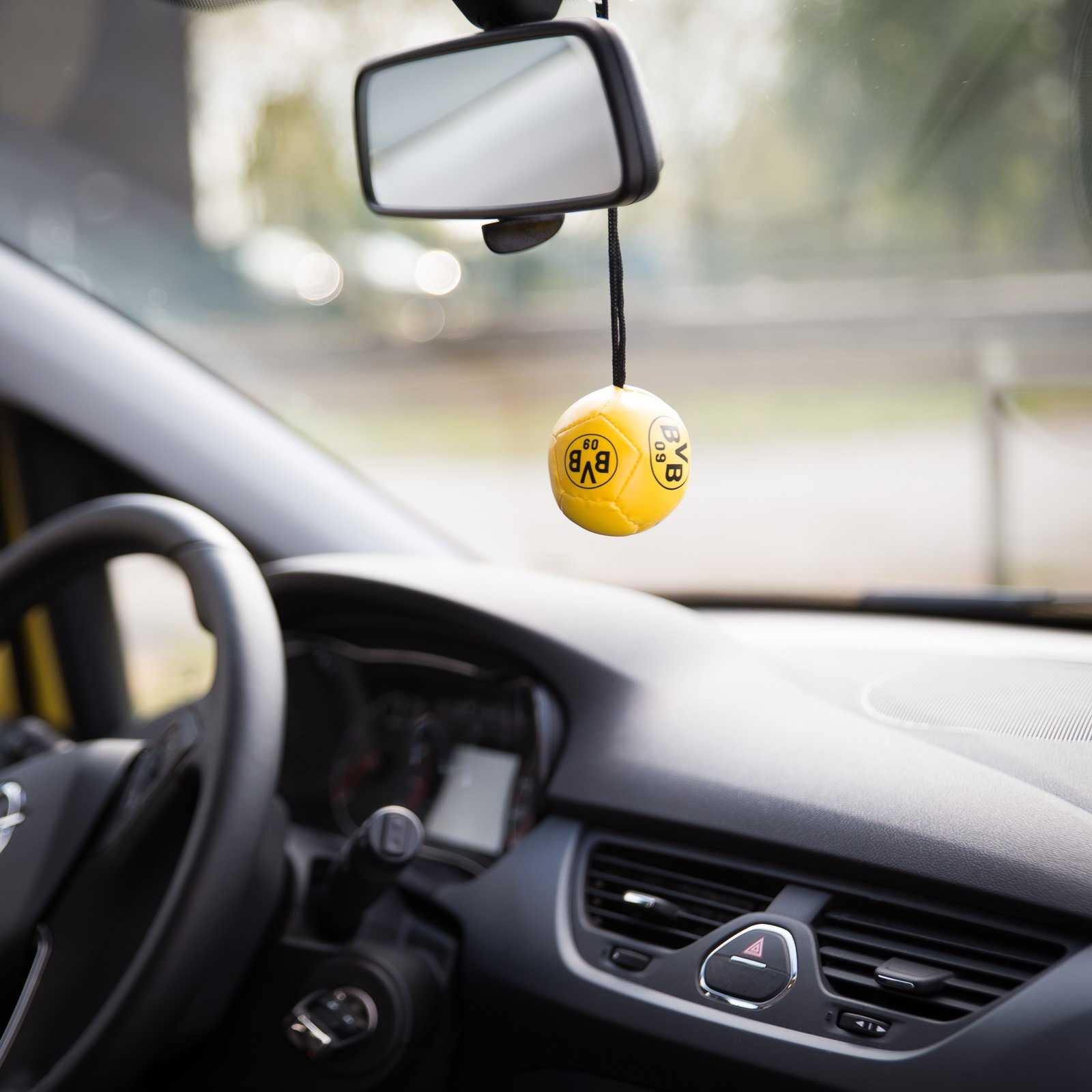 Detailansicht des gelben BVB-Autospiegelballs mit BVB-Emblem, hängend am Rückspiegel im Auto-Innenraum.