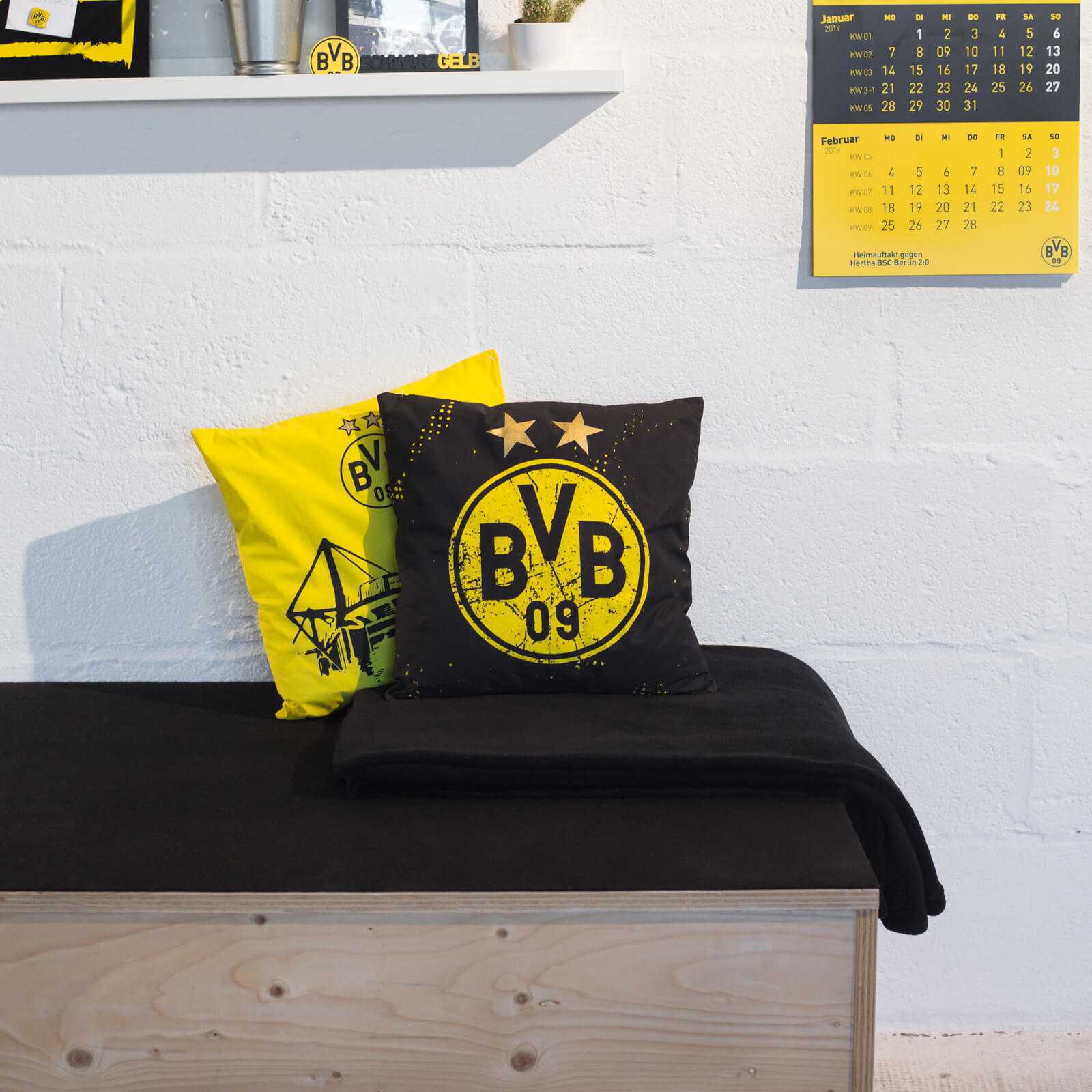 Vorderansicht von zwei BVB-Kissen Sterne in schwarzgelb, beide mit BVB-Emblem und Sternen, auf einer schwarzen Bank liegend.