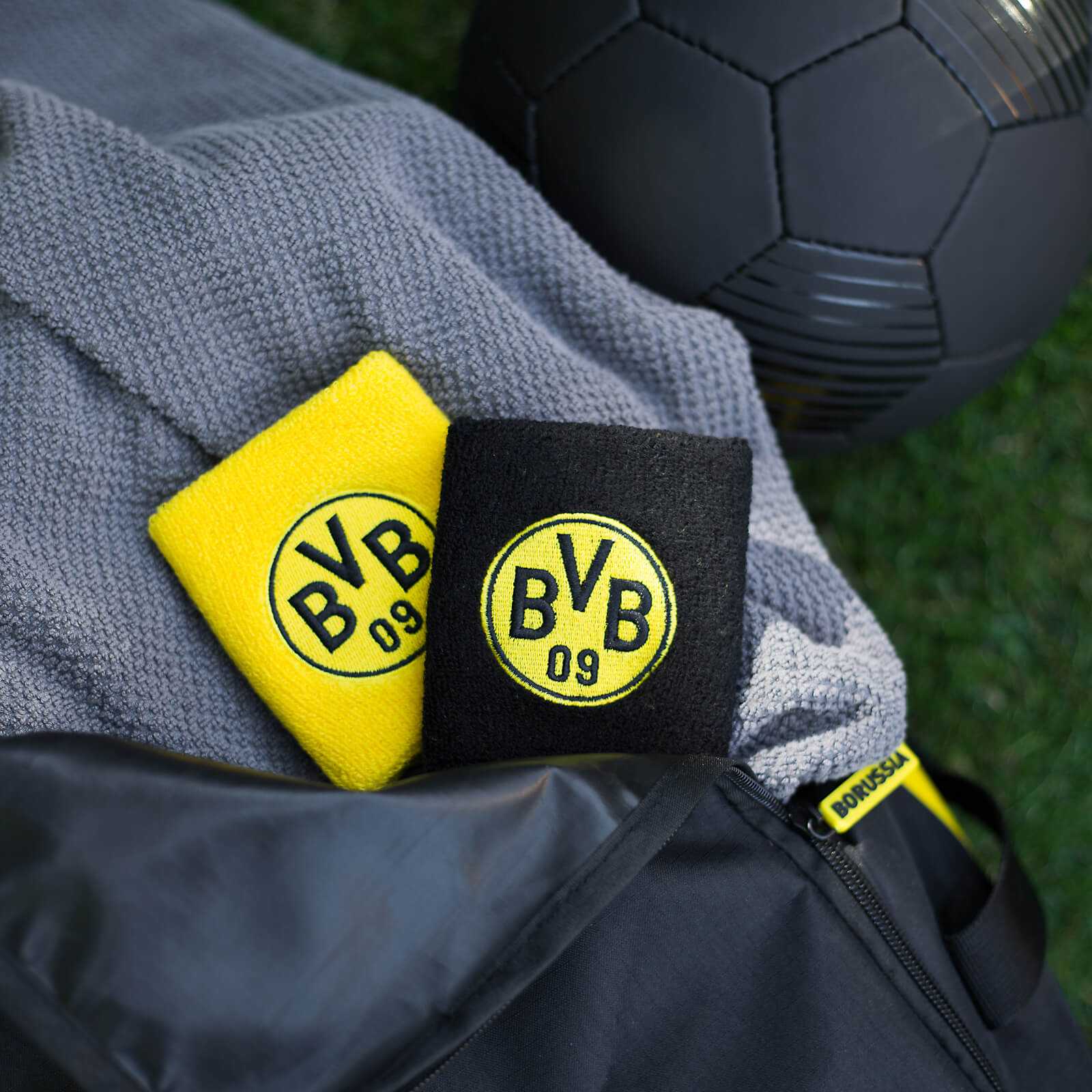 Nahaufnahme des BVB-Schweißband (2er-Set) mit einem gelben und einem schwarzen Band, jeweils mit BVB-Emblem, auf einer grauen Sporttasche.