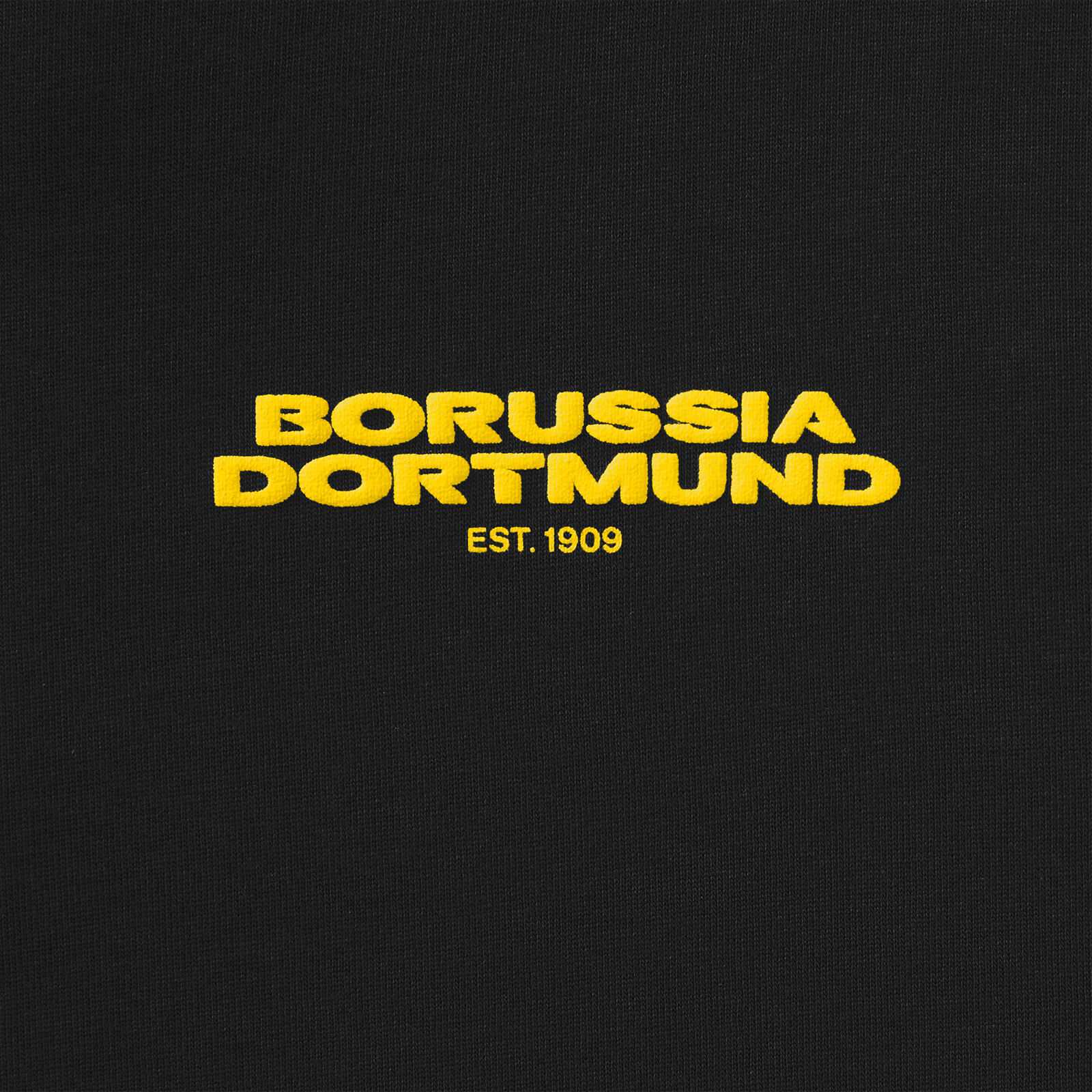 Detailansicht des anthrazitfarbenen BVB Urban Tee mit auffälligem gelbem "BORUSSIA DORTMUND EST. 1909" Schriftzug auf der Brust.