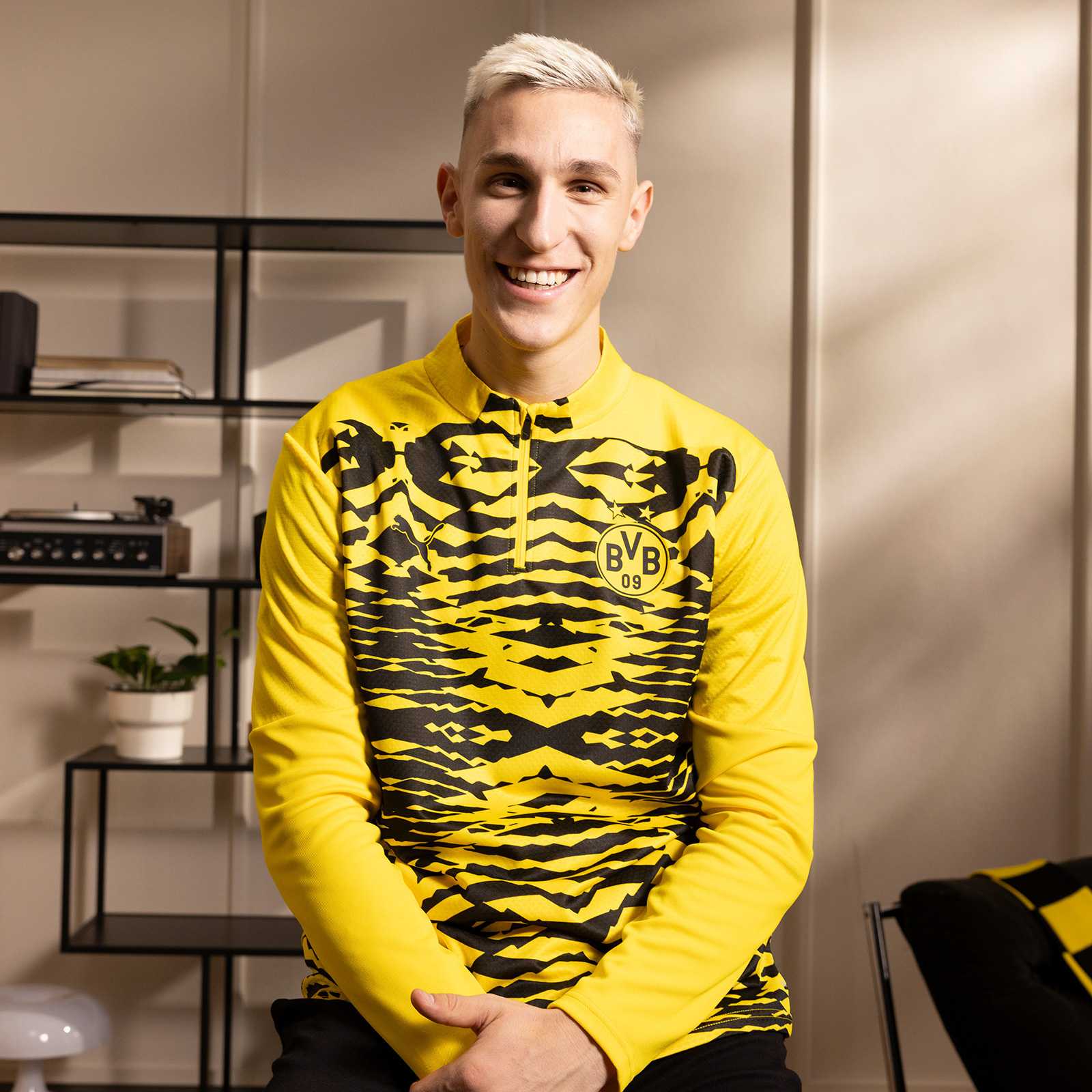 Frontalansicht eines Mannes, der das BVB Prematch Sweat schwarzgelb mit auffälligem Muster und BVB-Emblem auf der Brust trägt.