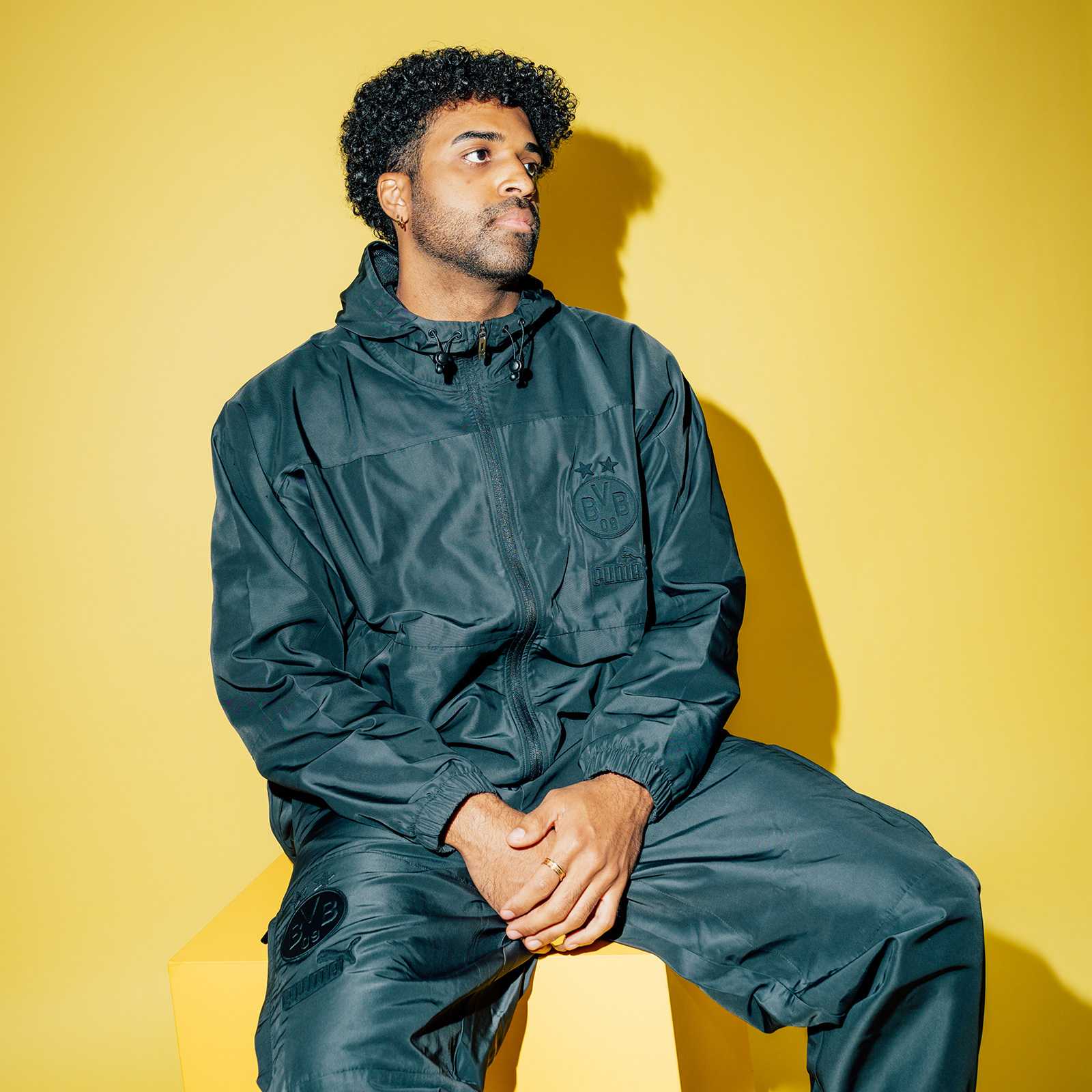 Frontalansicht eines Mannes, der die BVB Ftbl Monochrome Zipjacke und passende Hose trägt. Sichtbar sind BVB-Emblem und Puma-Logo auf der schwarzen Jacke.