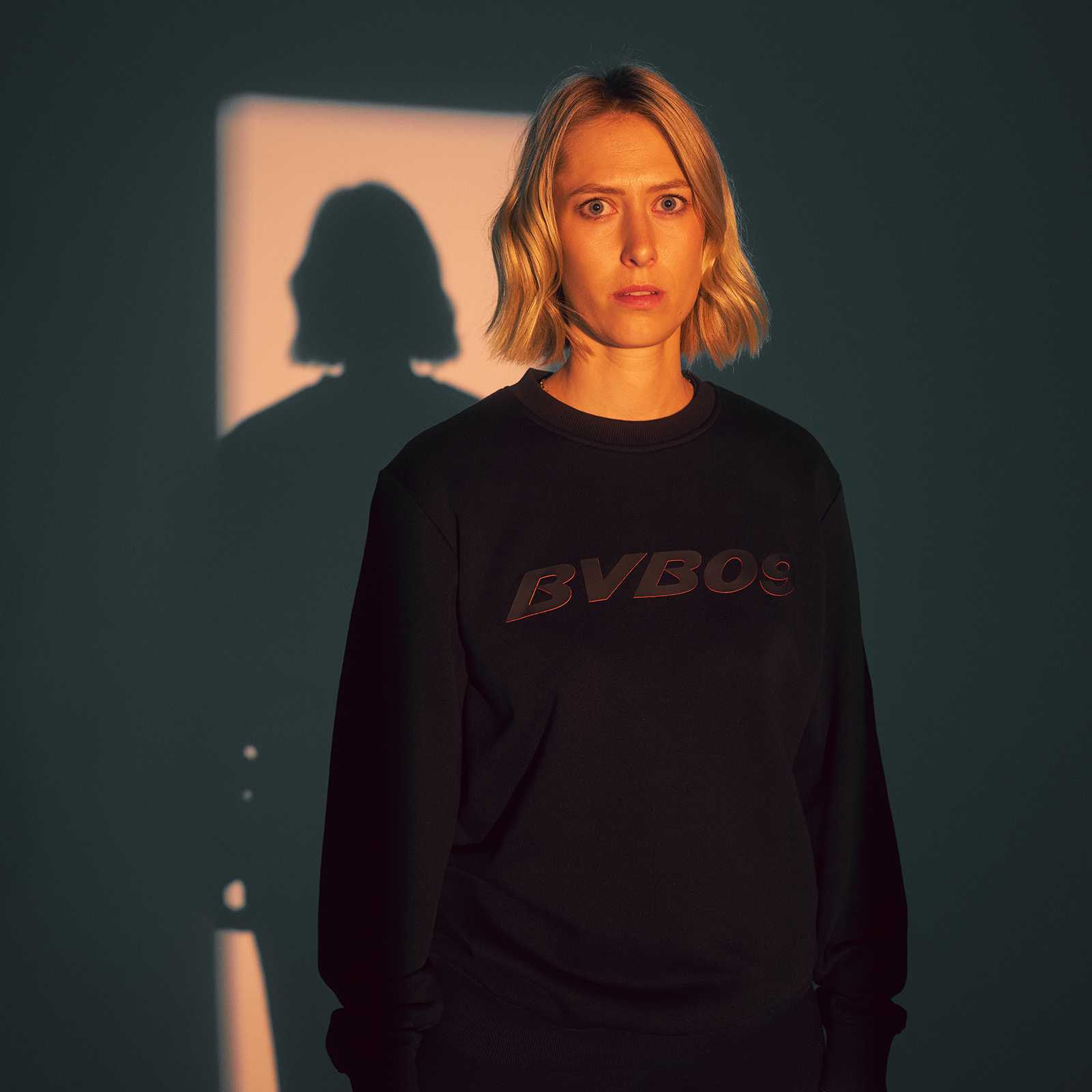 Frau trägt den schwarzen BVB Pullover Heat in der Vorderansicht; auffälliger „BVB09“-Schriftzug auf der Brust, schlichtes Design ohne weiteres Branding.