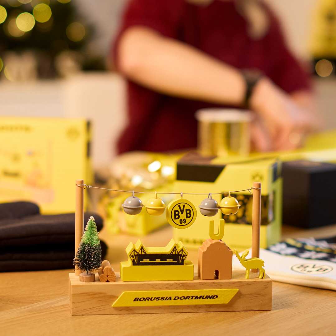 Detailansicht des BVB Holzstadion mit schwarzgelben Elementen, BVB-Emblem und Dortmunder Motiven auf einem Tisch, im Hintergrund eine Person.