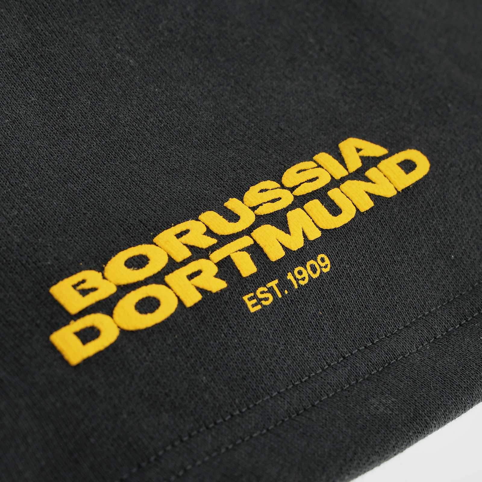 Detailansicht der BVB Urban Shorts anthrazit 2025 mit gelbem "Borussia Dortmund EST. 1909"-Schriftzug auf schwarzgelbem Stoff.