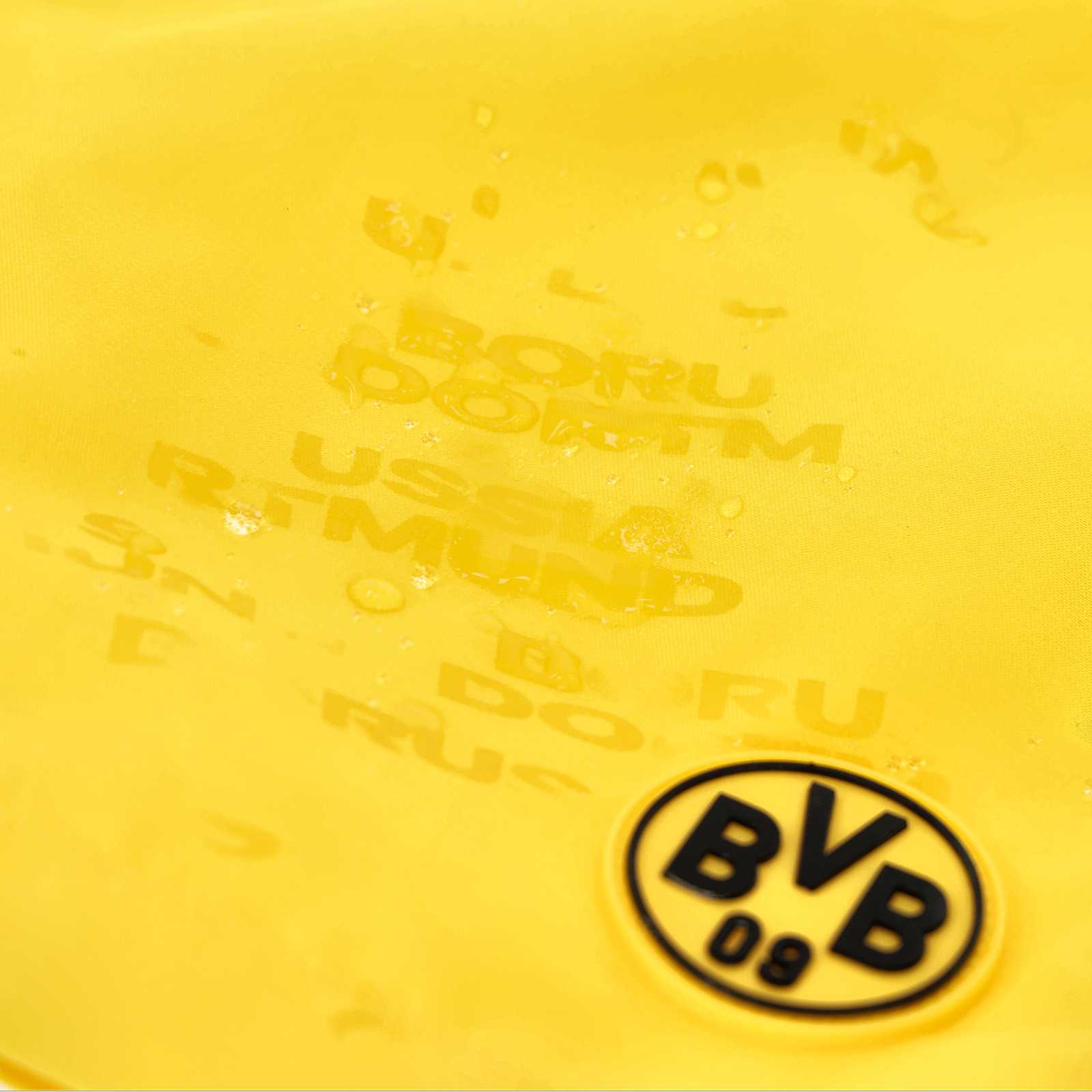 Detailansicht der gelben Reactive Badehose Kinder mit BVB-Emblem und geprägtem Borussia Dortmund-Schriftzug, Wassertropfen sind sichtbar.