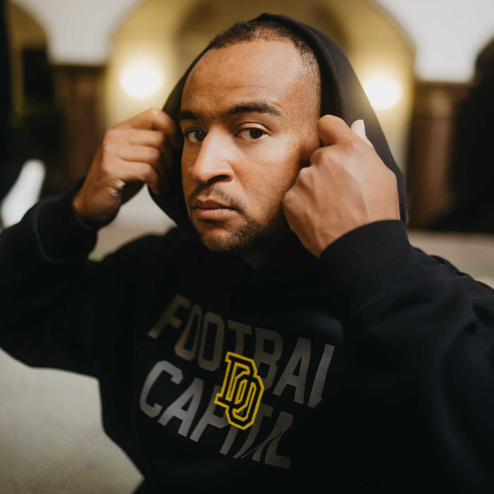 Nahaufnahme eines Mannes, der den schwarzgelben BVB College Hoodie trägt und die Kapuze aufsetzt. Frontansicht mit grauem "Football Capital"-Schriftzug.