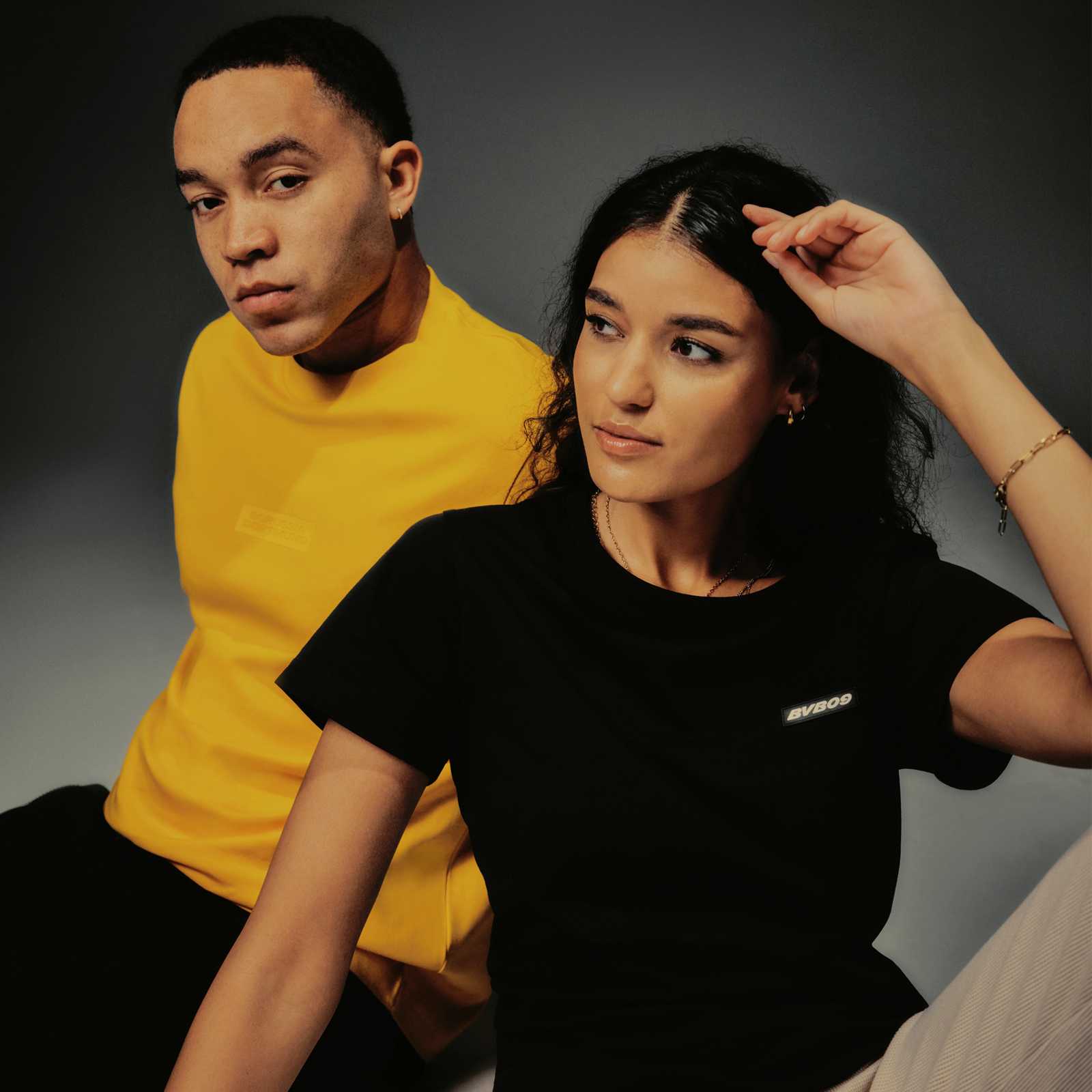 Ein weibliches Model trägt das schwarze T-Shirt, ein männliches Model trägt das gelbe T-Shirt