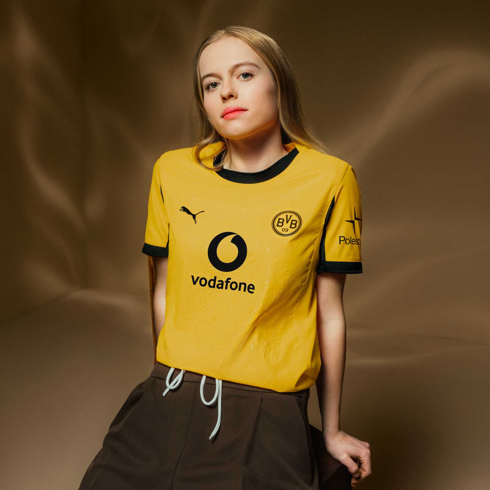 Ein weibliches Model trägt das gelbe Cuptrikot mit schwarzem Vodafone-Logo, PUMA-Katze und Retro-BVB-Emblem auf der Brust