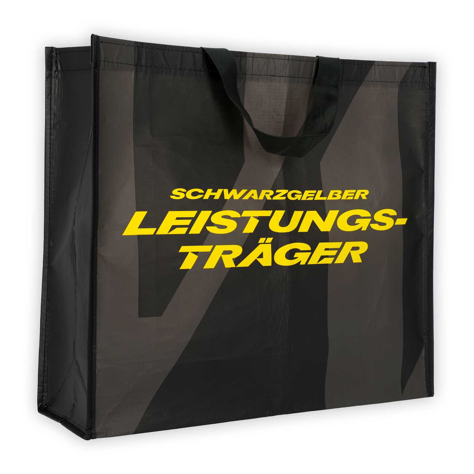 Schwarze Geschenktüte mit Henkeln und gelber Aufschrift.