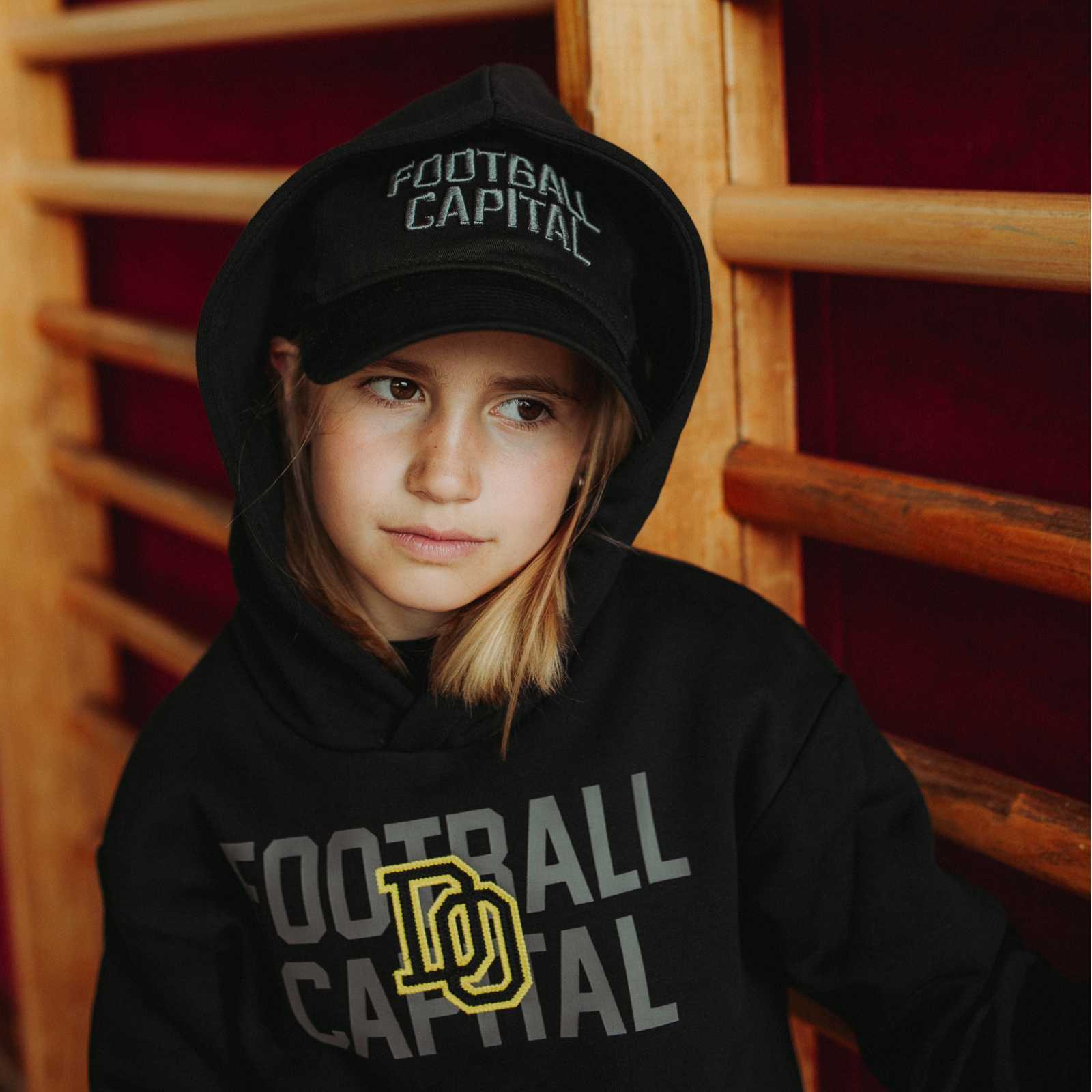 Ein Kinder-Modell mit schwarzem Hoodie trägt die schwarze Kappe unter einer Kapuze