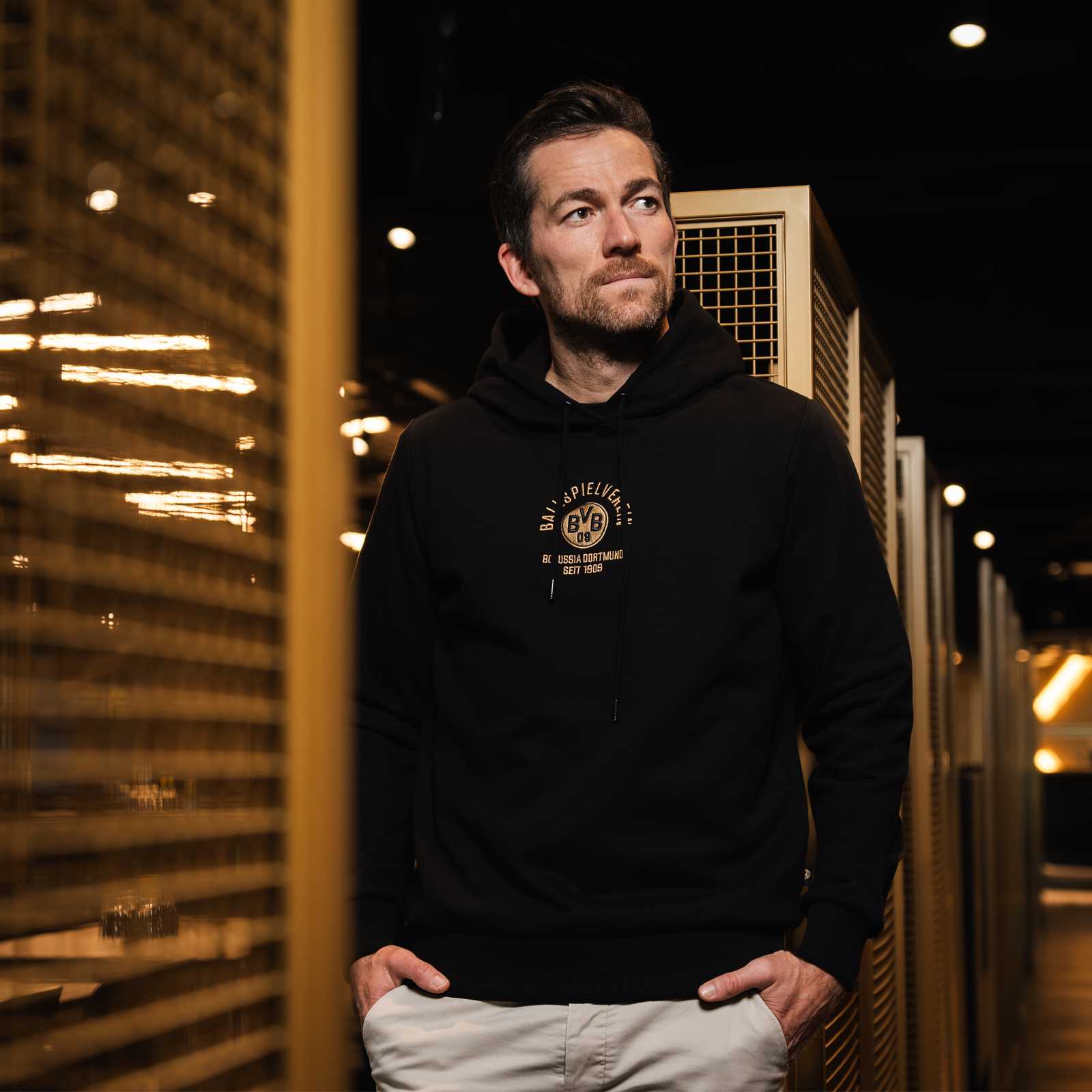 Ein männliches Model mit Bart trägt den schwarzen Hoodie