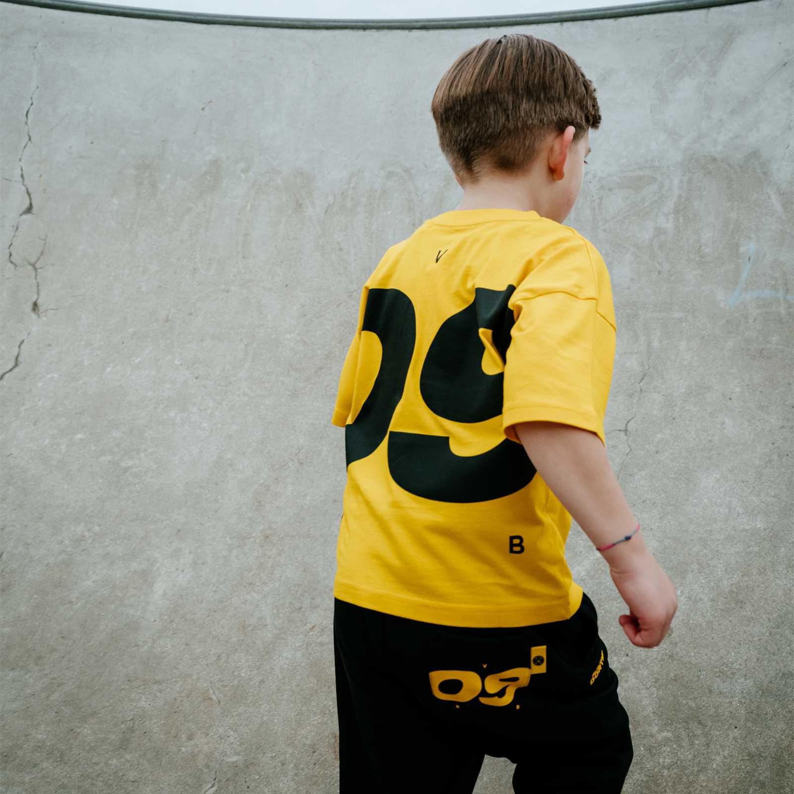 Kleiner Junge in gelbem BVB-Shirt mit großem 09-Print in schwarz auf der Rückseite läuft vor der Kamera weg.