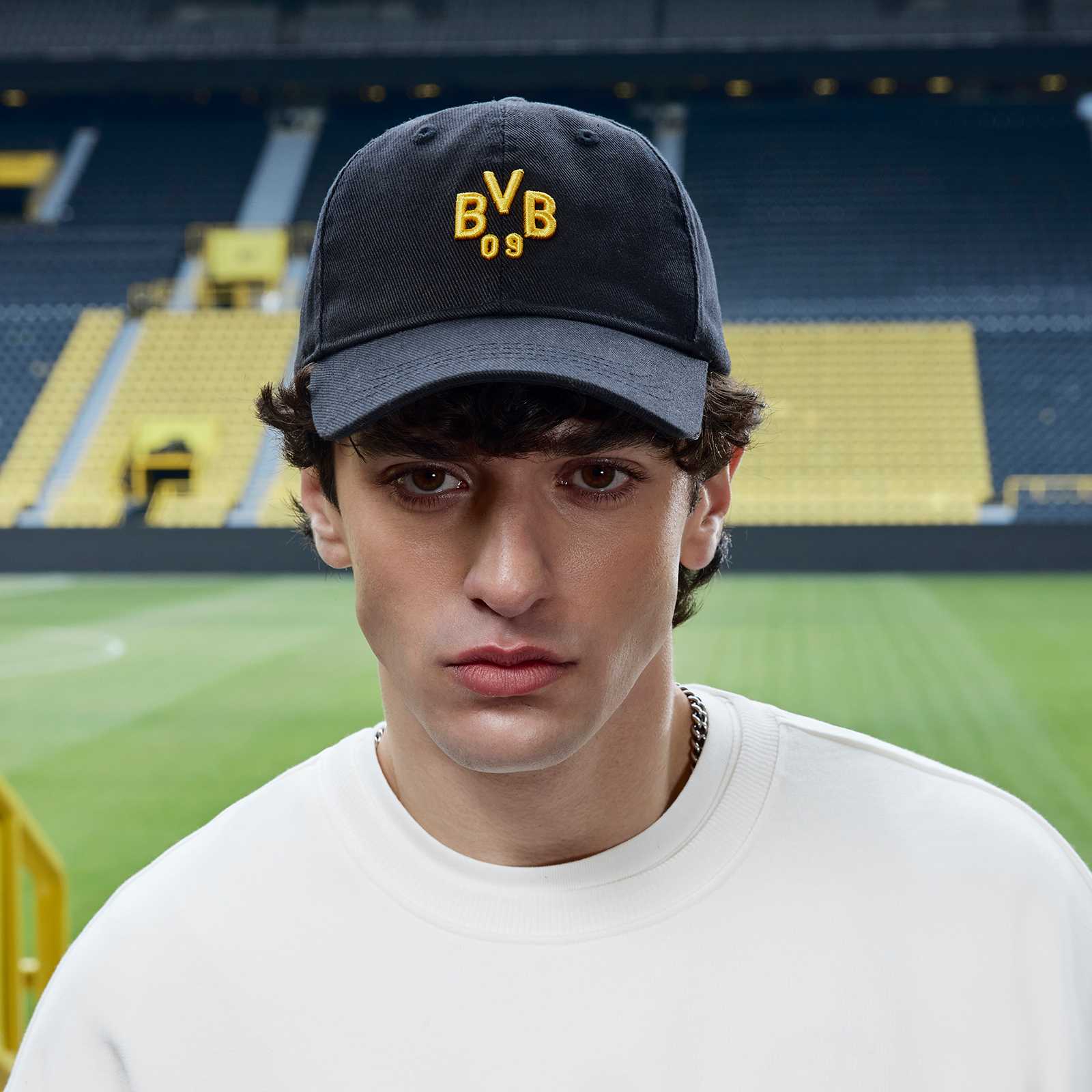 Ein männliches Model im Stadion trägt die Kappe und schaut in die Kamera