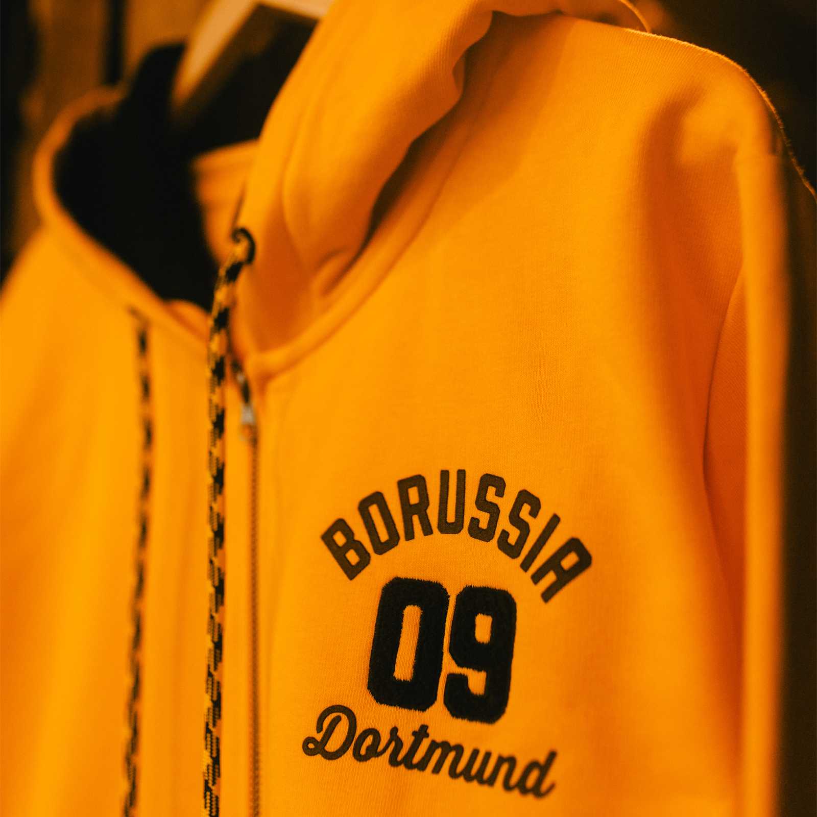 Seitliche Ansicht der gelben BVB-Jacke die an einem Bügel hängt.