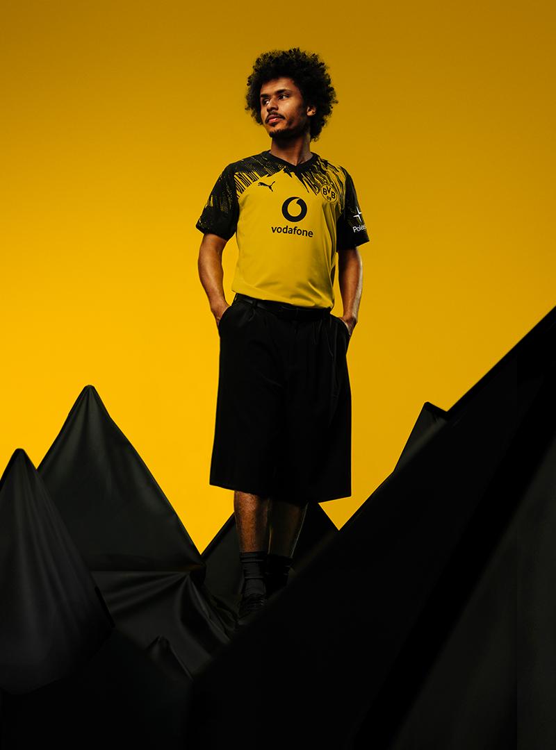Adeyemi im gelben BVB Heimtrikot 25/26 vor gelbem Hintergrund