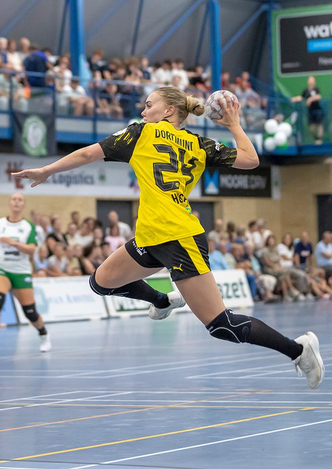 Handballerin im Heimtrikot 25/26 die auf dem Handballfeld zum Wurf ausholt.
